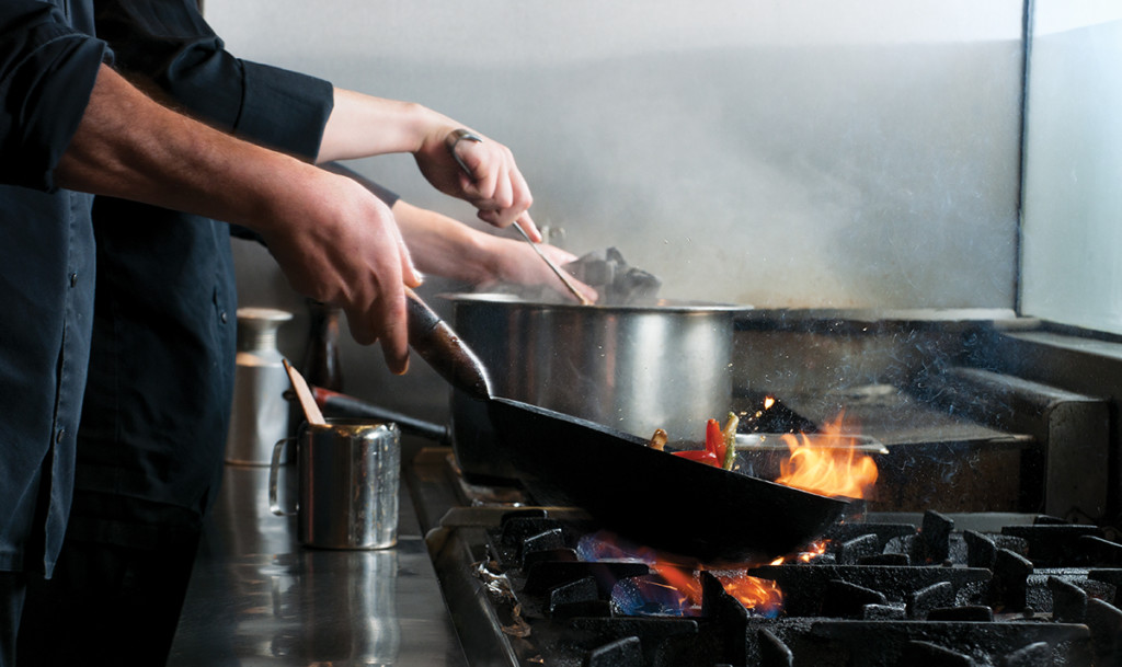 chef flambe vegetables in frying pan on stove in commercial kitchen